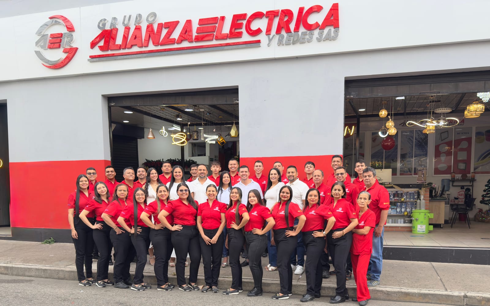 El equipo completo de Grupo AER, con camisetas rojas y blancas, reunido frente a la fachada de la sede en Bucaramanga bajo el letrero de Grupo Alianza Eléctrica y Redes