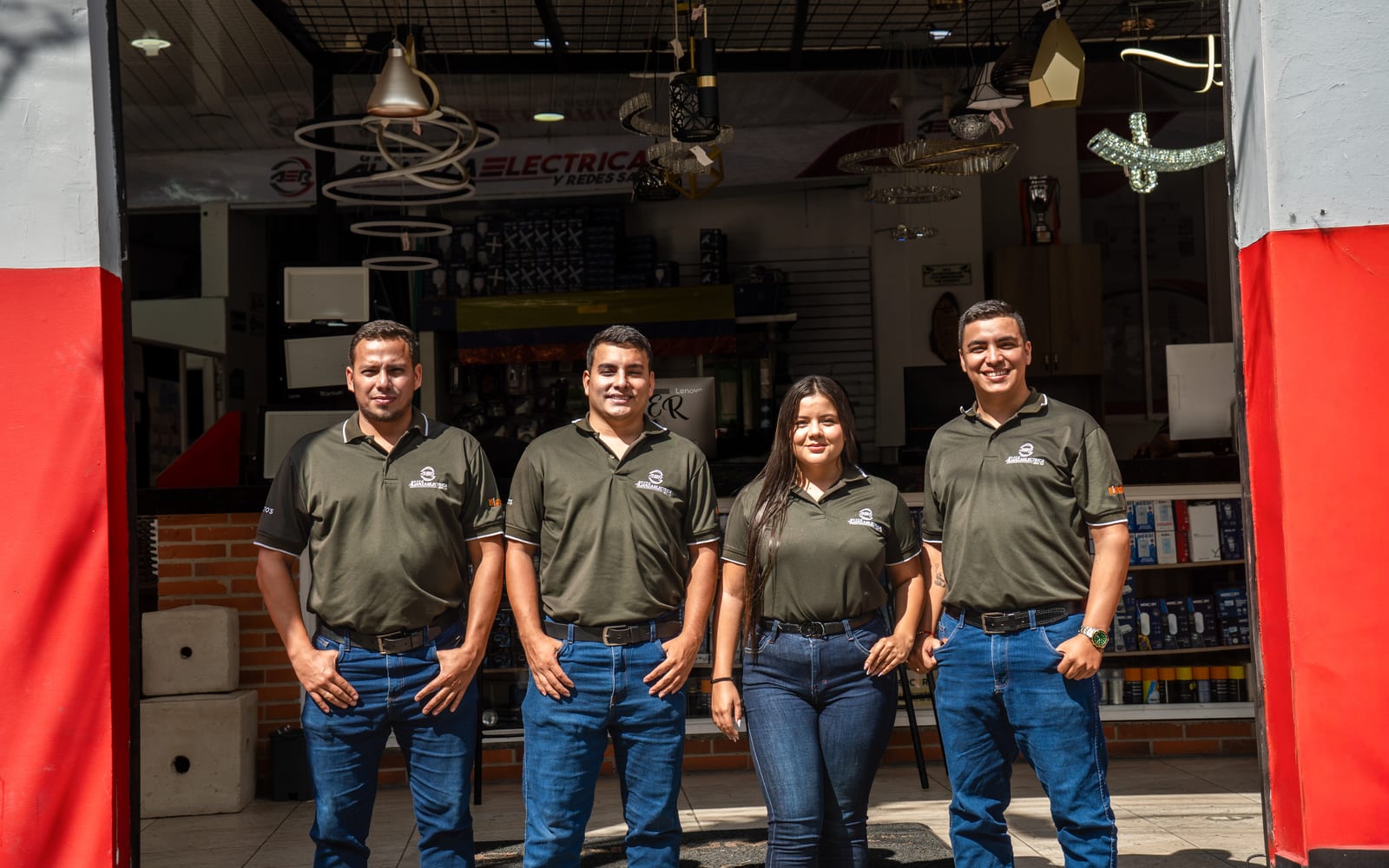 Cuatro integrantes del equipo de Grupo AER, con el uniforme corporativo, en la entrada de la sede de Bucaramanga con la exhibición de iluminación al fondo